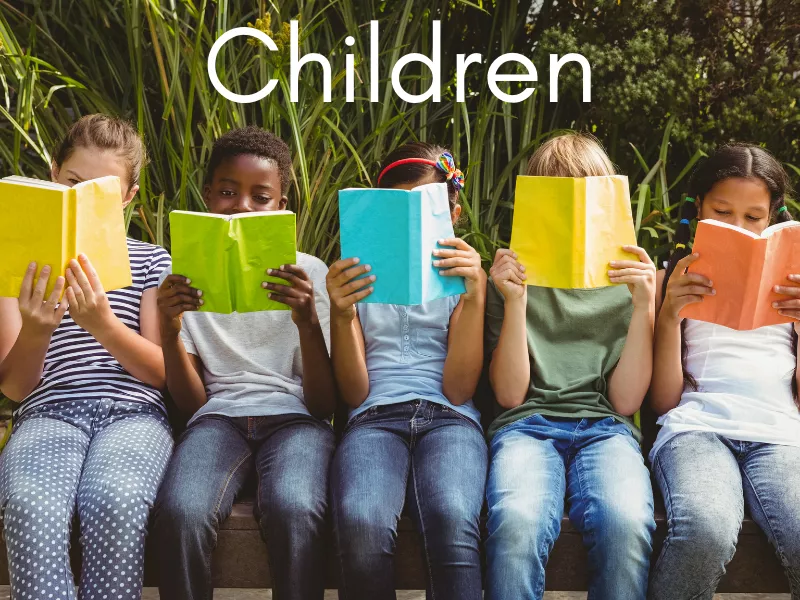 Five children of different races reading while sitting on a bench outside.  